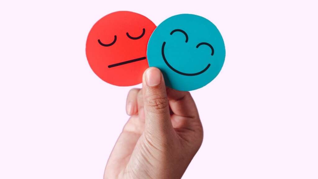 A hand holding to circular pieces of paper. One with that is red with a sad face, the other that is blue with a happy face (1)