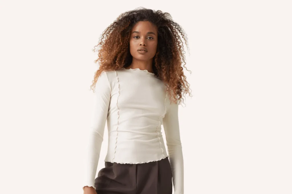 Model with long curly hair wears fitted frill top and dark brown trousers. Autumn High Street Finds