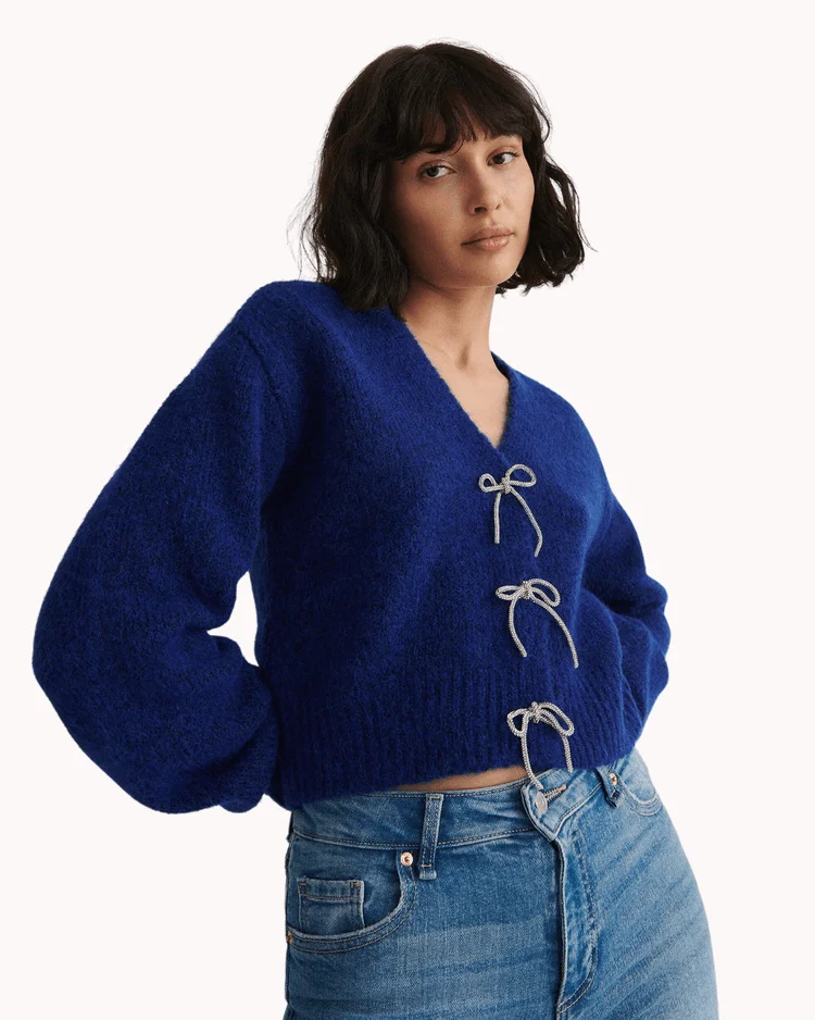 Model poses wearing blue cardigan with bow fasteners