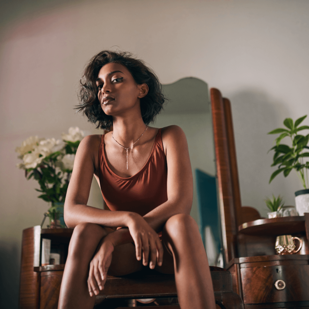 Strong woman sitting down in a dimly lit room staring at the camera. How to radiate feminine energy