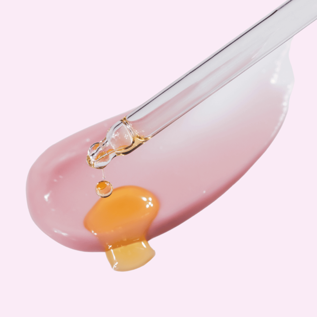 Cosmetic Pipette with Drops of Oil and Pink Cream Smear on a Pink Background