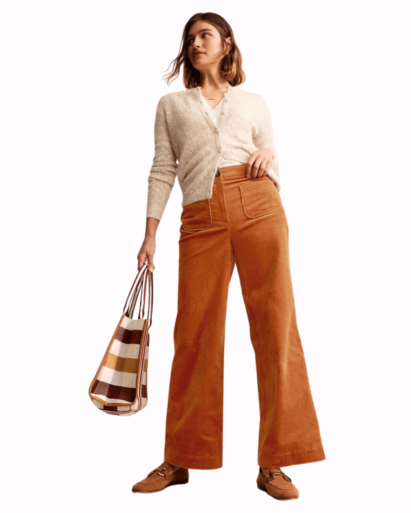 Model wears orange corduroy trousers and a cream cardigan