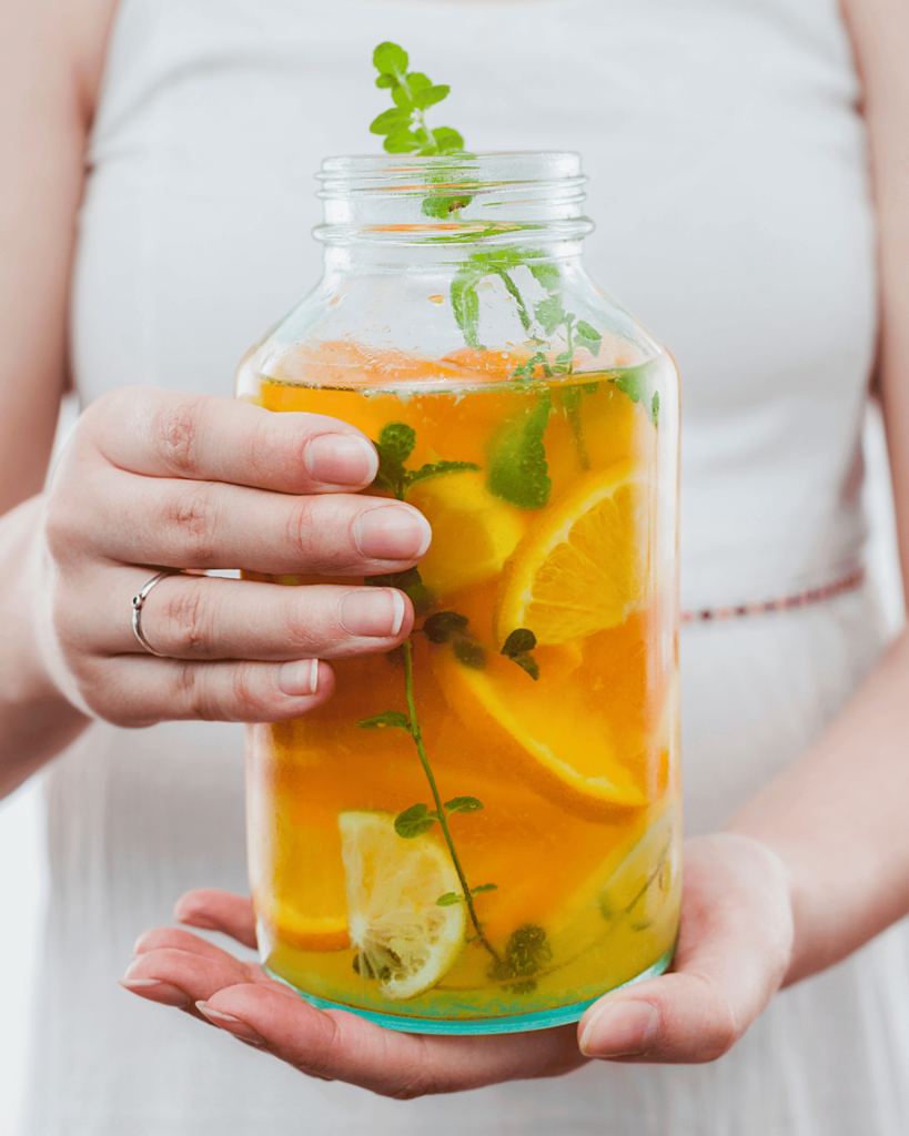 Upclose shot of woman holding a large jar of orange and lemon infused water. 9 Ways To Stay Hydrated (That Isn’t Water)