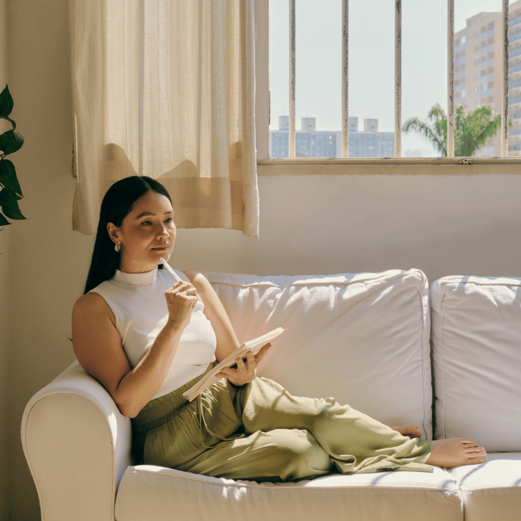 Woman sits on her cream coloured sofa writing in her journal