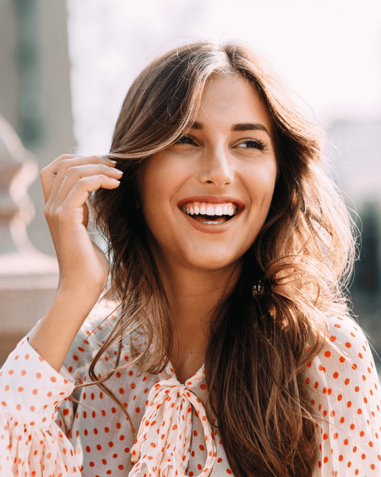 Woman smiles looking away from the camera, she wear a polka dot top