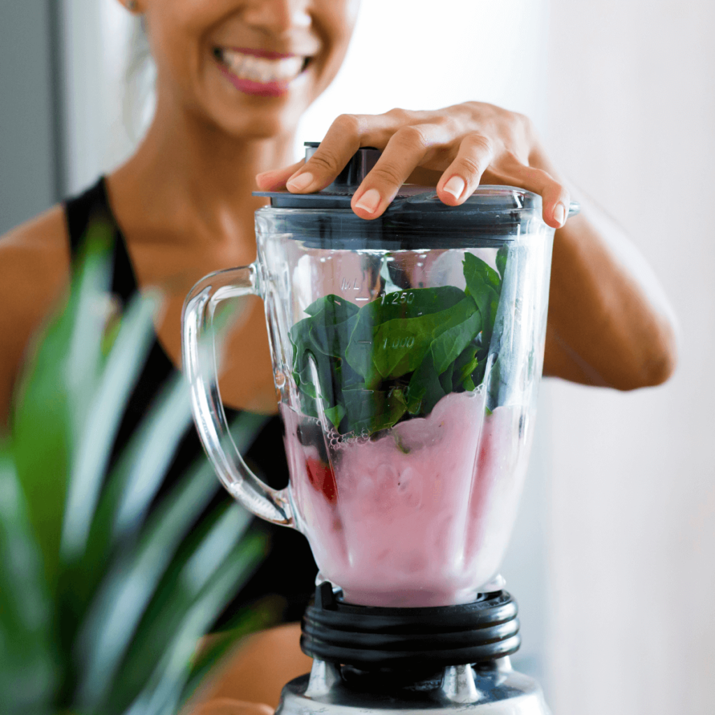 Woman smiling as she makes a berry and spinach smoothie