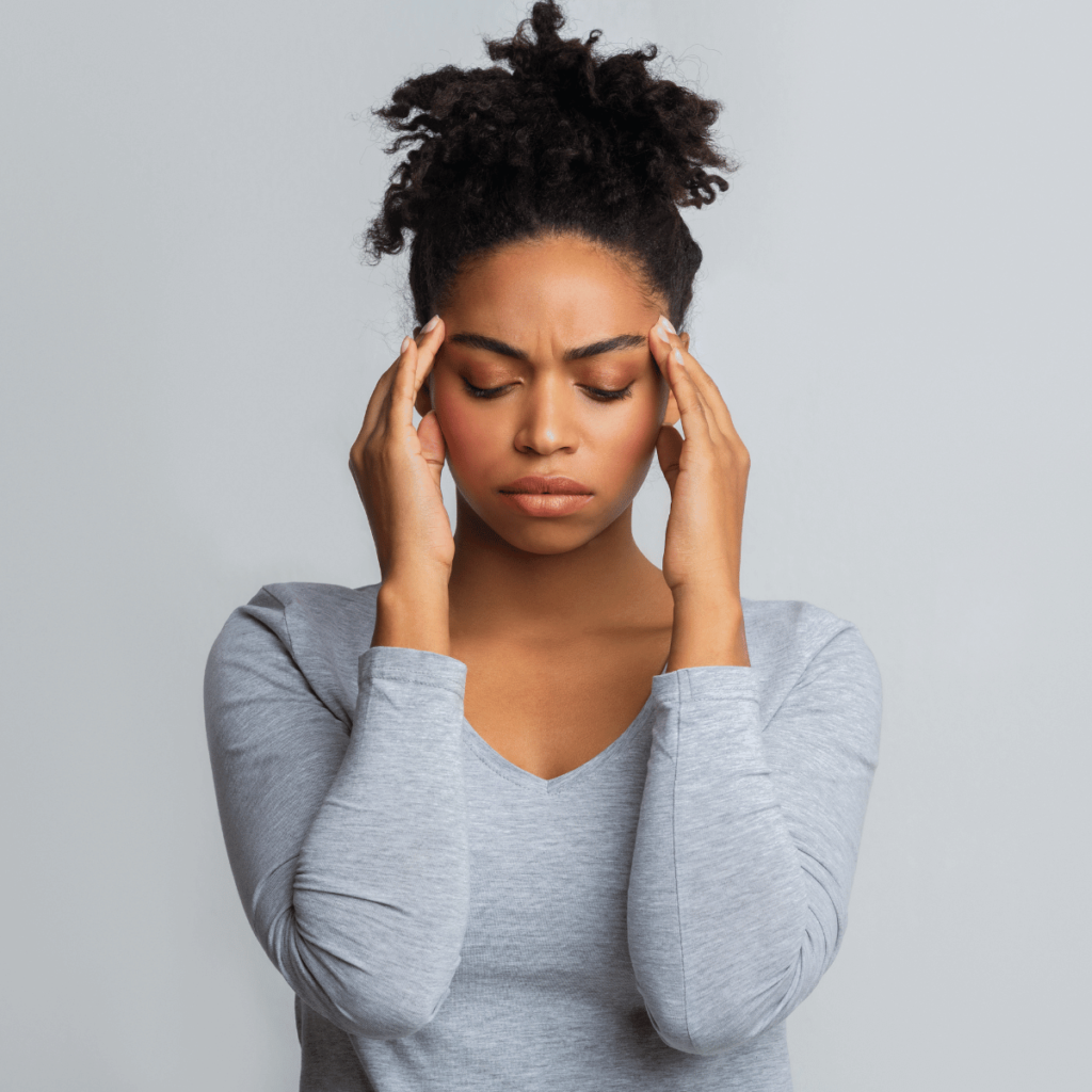 medium shot of woman placing her hands either side of her head indicating a headache