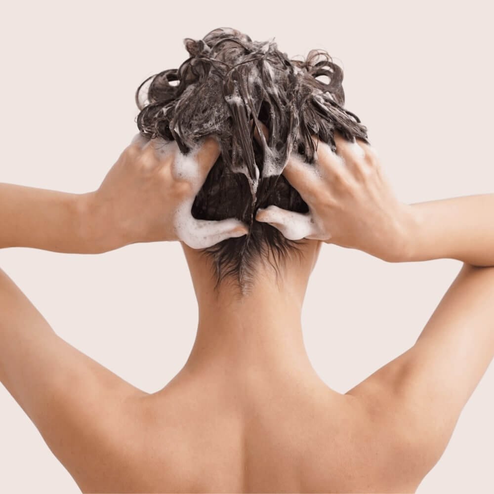 Back view of a woman shampooing her hair. Clove Oil For Hair Growth