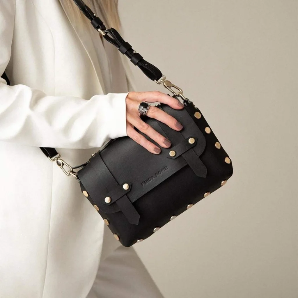 Women in a off-white blazer wearing a black vegan leather crossbody bag. Vegan Luxury Brands