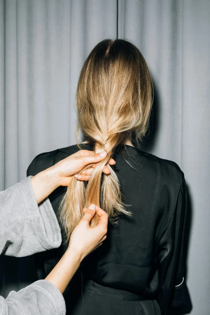 backview of woman plaiting someone's blonde hair. Remove Green Tones From Bleached Hair