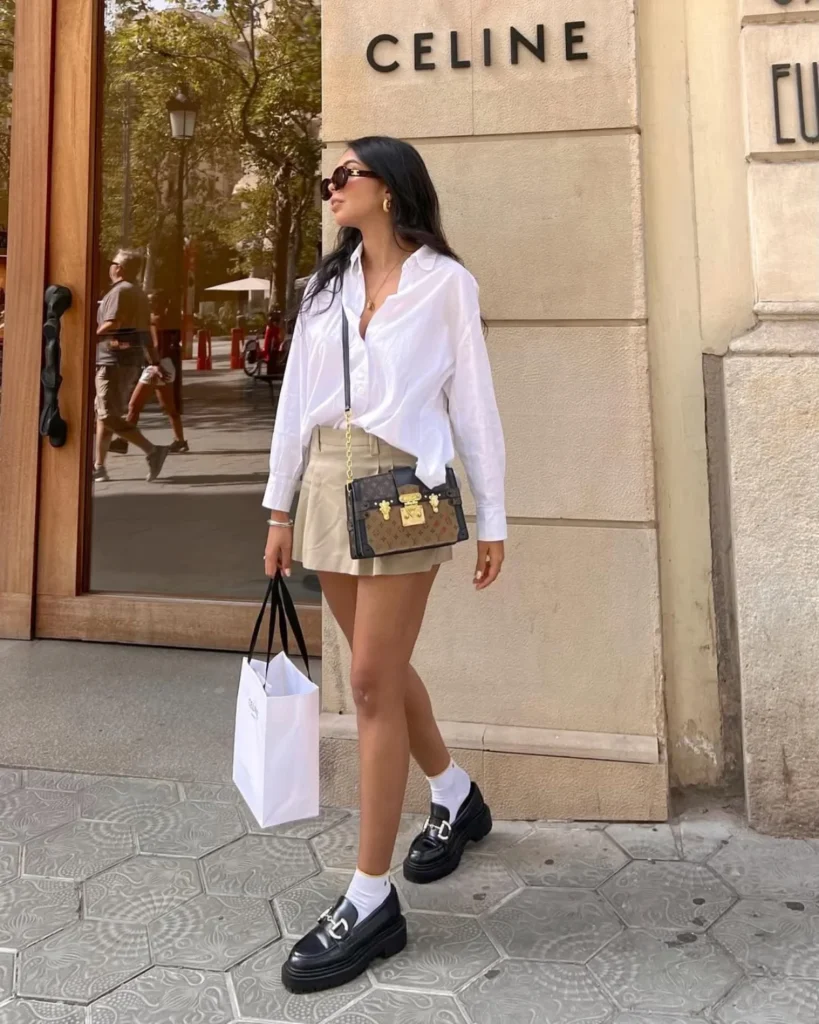 Yourng woman with black hair wearing a white blouse and cream mini skirt and crossbody bag. Old Money Outfit Ideas