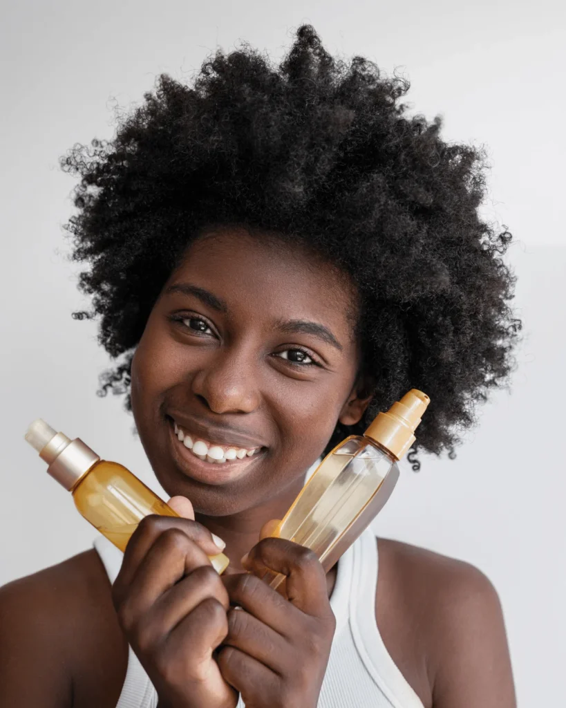 beautiful black woman with an afro holding two bottles of hair oil. Fast Hair Growth Tips for Low Porosity Hair